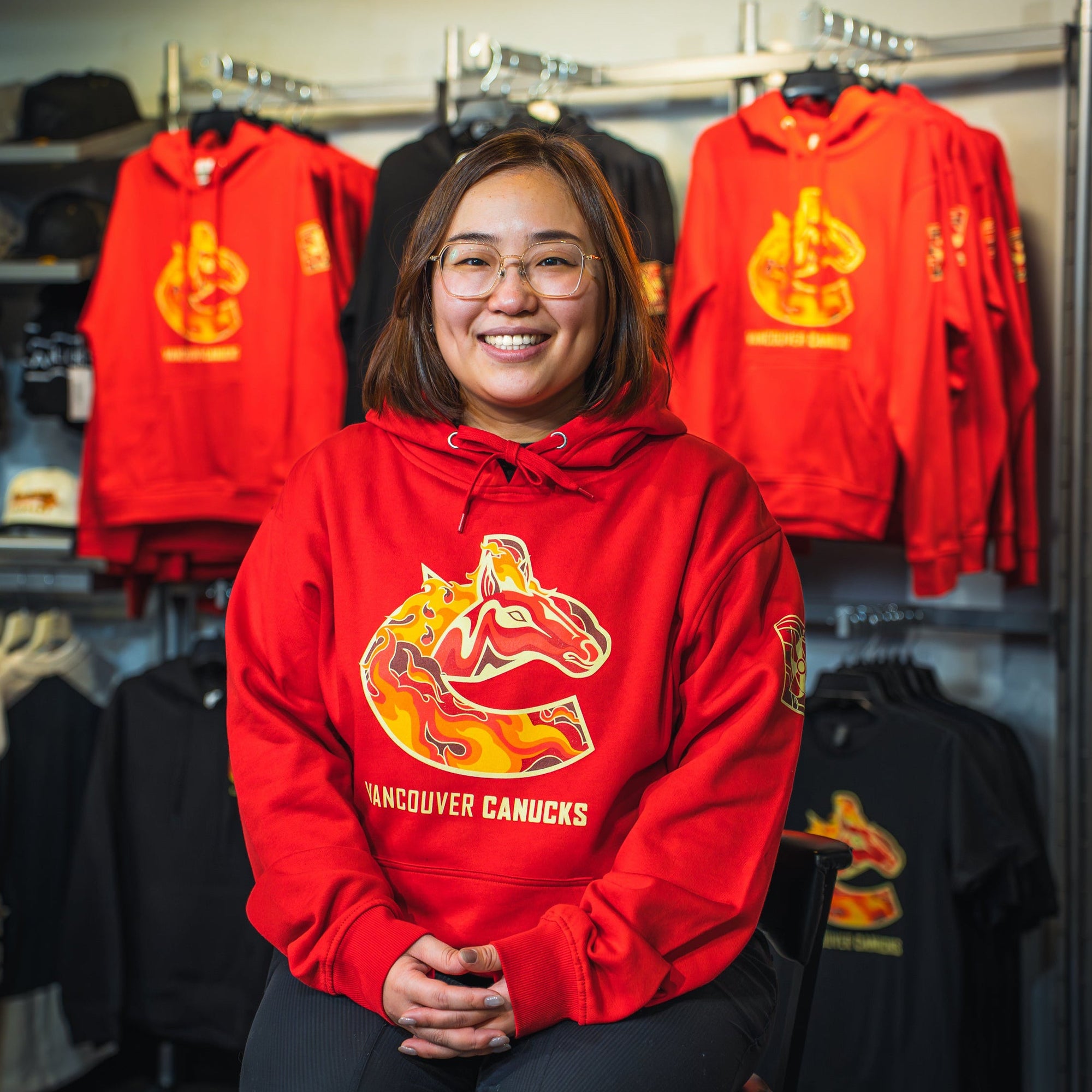 Person wearing a red Vancouver Canucks hoodie in a store with sports merchandise.