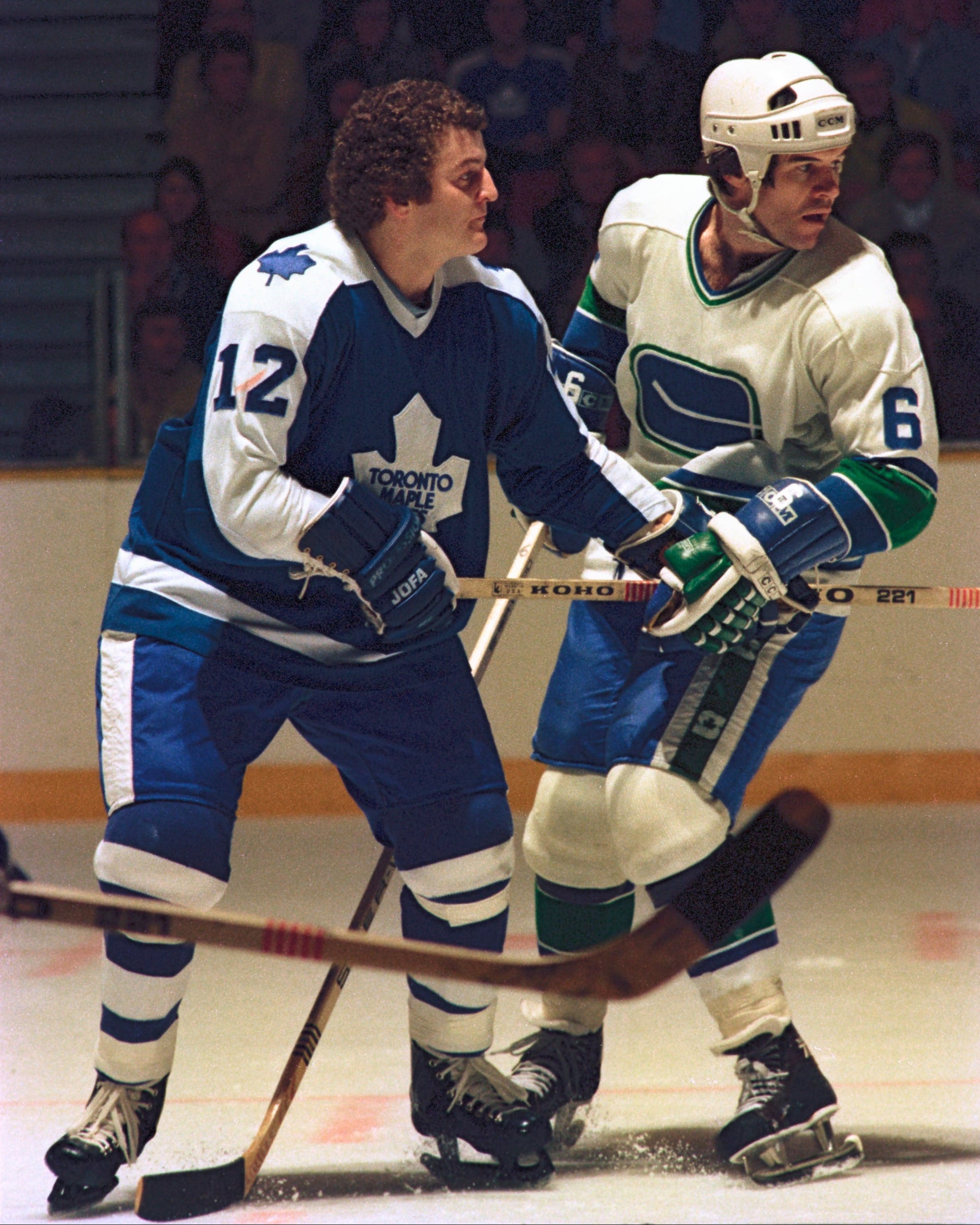 Two hockey players in action on an ice rink with a crowd in the background